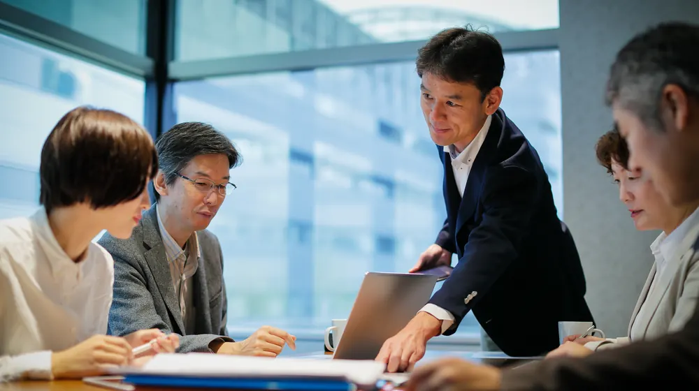 会議室で経営陣に資料を示しながら説明する登壇者